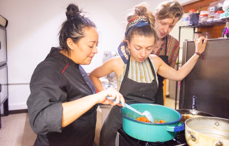 a younf woman listening and watching a female chef explain cooking techniques